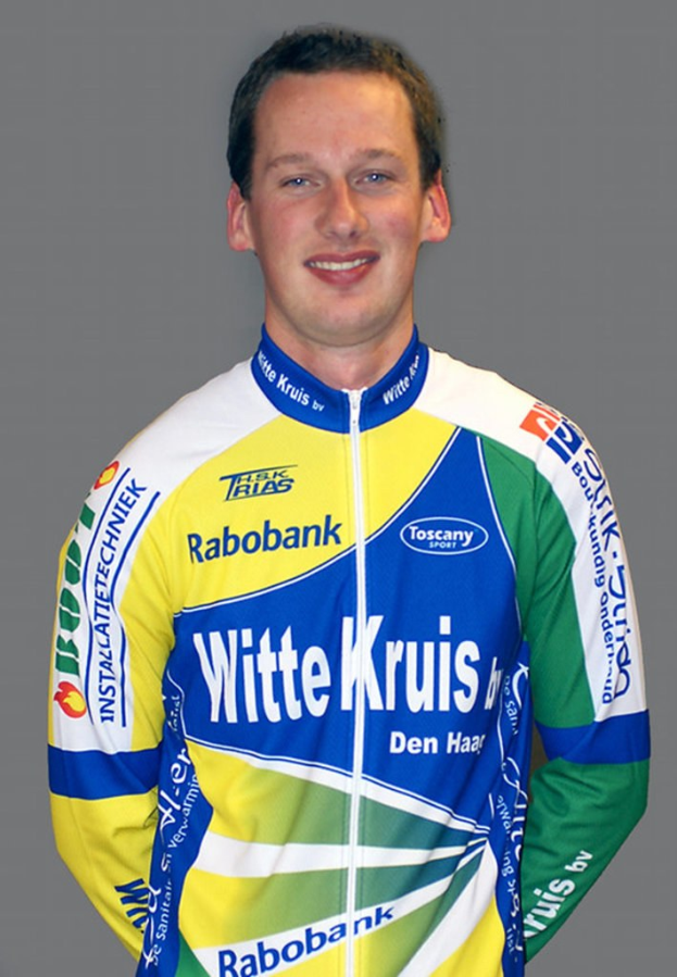 Ein männlicher Sportler posiert für ein Foto, wobei er ein Hemd trägt, auf dem mehrere Sponsorunternehmennamen zu sehen sind.