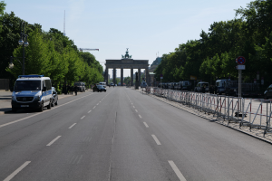 Ein Polizeiwagen steht auf der Seite einer vielbefahrenen Straße vor dem Brandenburger Tor in Berlin, Deutschland, mit Bäumen, Laternenmasten, Absperrungen und Schildern im Hintergrund und einer bewölkten Himmel.