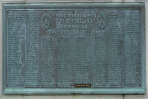 Metallplakette an einer Gebäudewand mit "Denkmal für die Stadt Portland" in fetter schwarzer Schrift, umgeben von einem dekorativen Rahmen.