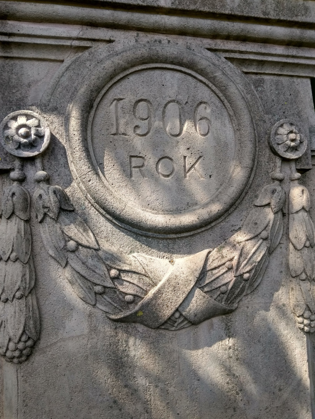 Nahaufnahme eines steinernen Denkmals mit einem Kranz und eingravierter Inschrift.