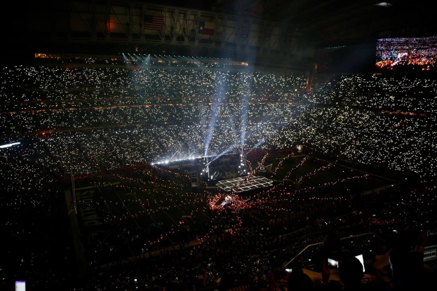Eine große Menge Menschen in einem hell erleuchteten Stadion bei Nacht schaut auf einen Bildschirm, der die Ergebnisse der Super Bowl XLVII-Halbzeitshow anzeigt.