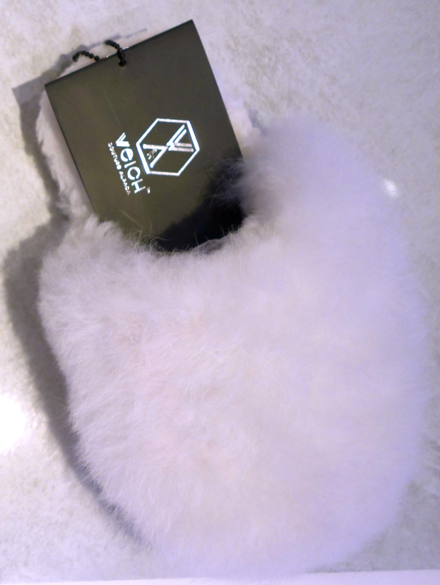 Ein weißer Pelzbeutel mit einem schwarzen Etikett, aus Schafsfell gefertigt, auf einer weißen Oberfläche sitzend.