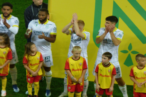 Eine Gruppe von Fußballspielern in Uniformen klatscht feiernd auf einem Ligue 1-Feld, mit einem "Ligue 1"-Schild im Hintergrund.